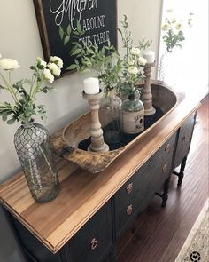 a wooden table topped with vases filled with white flowers and greenery next to a mirror