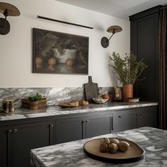 a kitchen with marble counter tops and black cupboards, an art work on the wall