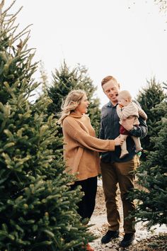 a man and woman are holding their son in the middle of a christmas tree farm