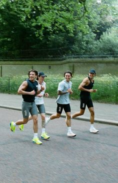 three men running down the street in front of some trees and bushes, with one man wearing