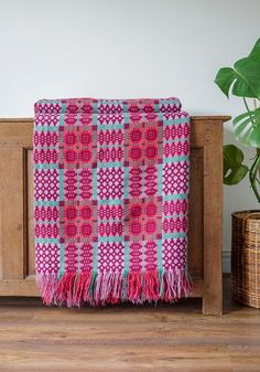 a pink and blue blanket sitting on top of a wooden table next to a potted plant