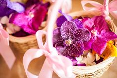 two baskets filled with purple and pink flowers on top of a wooden table next to ribbons