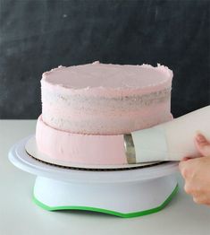 a person using a knife to cut a cake with pink frosting on top and white icing on the bottom