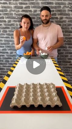 a man and woman standing next to a table with an egg carton on it