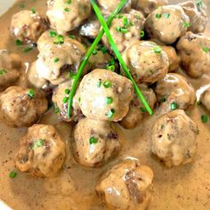 a bowl filled with meatballs covered in gravy and garnished with green chives