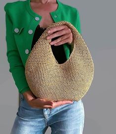 a woman in green jacket holding a woven purse over her shoulder and looking at the camera