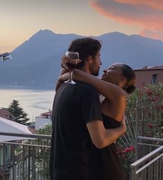 a man and woman standing next to each other on a balcony with mountains in the background