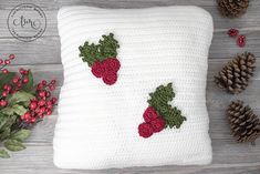 a crocheted strawberry pillow sitting on top of a wooden table next to pine cones