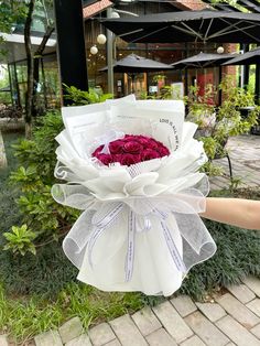 a person holding a bouquet of roses in front of a building with trees and bushes