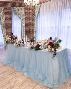 a long table with flowers on it in front of a brick wall and window curtains