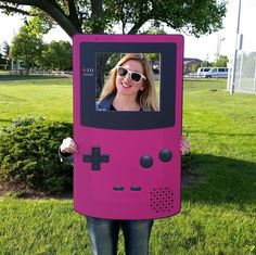 a woman holding up a pink gameboy costume in the grass with her eyes closed