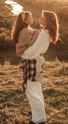 a woman holding a child in her arms while standing on top of a grass covered field