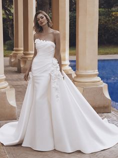 a woman in a white wedding dress standing next to a swimming pool with columns on either side