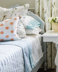 a white bed topped with lots of pillows next to a night stand and table filled with flowers