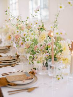 the table is set with white and pink flowers in vases, candles, and napkins