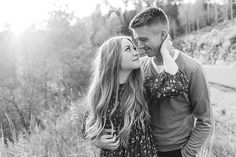 a man and woman standing next to each other in front of tall grass with trees behind them