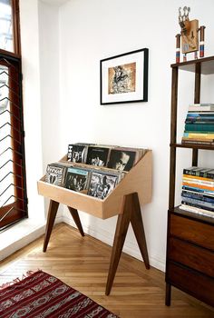 a wooden table topped with lots of books on top of a hard wood floor next to a window