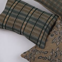 two decorative pillows sitting next to each other on a white surface, one is green and the other is brown