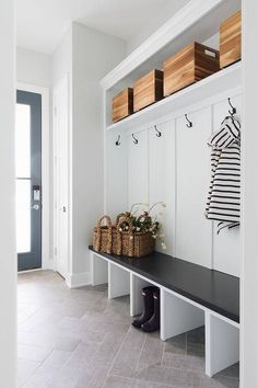 a bench with two baskets on it in front of a white wall and black door