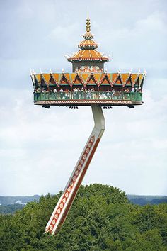 an amusement park ride with people riding on it's sides and trees in the background