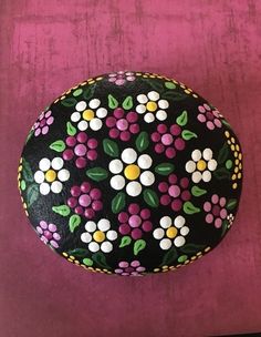 a painted rock sitting on top of a pink table next to a purple wall with white and yellow flowers