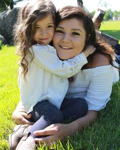 mother and daughter sitting in the grass smiling at the camera with their arms around each other