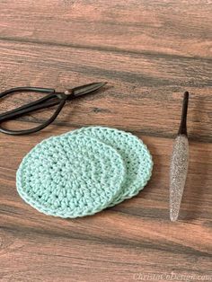 two crocheted coasters sitting on top of a wooden table next to scissors