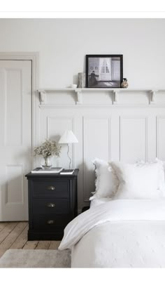 a bedroom with white bedding and pillows on the headboard, next to a night stand