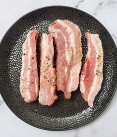 four pieces of bacon on a black plate with seasoning sprinkled around them