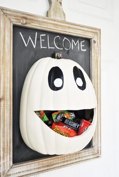 a white pumpkin with black eyes and mouth painted on it's side in front of a welcome sign