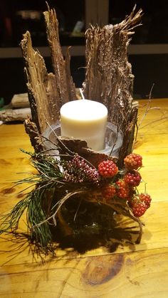 a candle that is sitting on top of some branches and berries in front of it