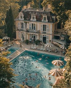 an aerial view of people swimming in a large pool surrounded by trees and umbrellas