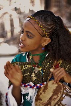 a woman in native clothing holding a drum and looking at the ground with her eyes closed