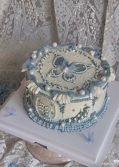 a blue and white cake sitting on top of a table next to a lace covered wall