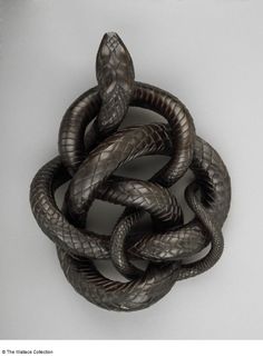 a metal snake on a white surface with it's head in the shape of a knot