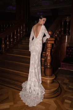 the back of a woman in a white dress standing on some stairs with her hands on her hips