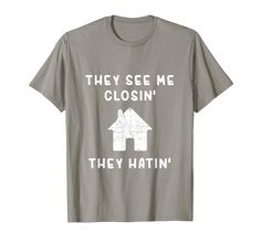 a grey t - shirt that says they see me close to the house with two houses on