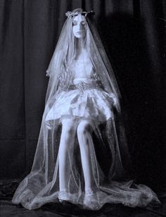 a mannequin dressed in a white dress and veil sitting on a black surface