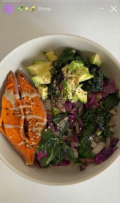 a white bowl filled with salad and dressing on top of a table next to a cell phone