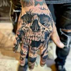 a hand with a skull on it that is covered in black ink and some other tattoos