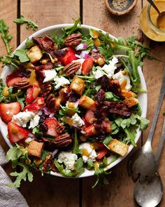 a salad with strawberries, bacon, and goat cheese in it on top of a wooden table