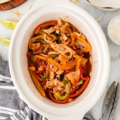 a white bowl filled with chicken and peppers on top of a table next to utensils