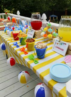 an outdoor party with yellow and white striped table cloths, plates, cups, bowls, drinks and decorations