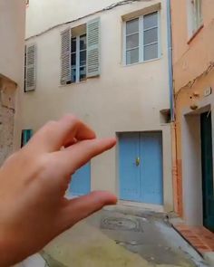 a person holding their hand out in front of a building with blue doors and shutters