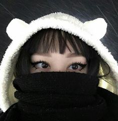 a woman wearing a white bear hat and black scarf with her eyes wide open while covering her face