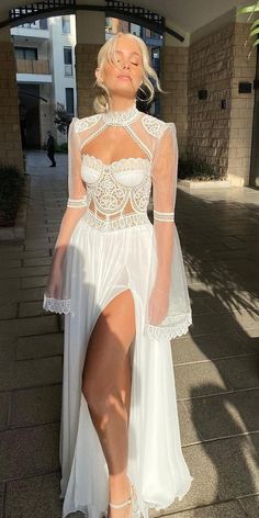 a woman wearing a white dress and high heels is standing on the sidewalk in front of a building