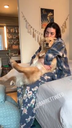 a woman sitting on top of a bed holding a brown and white dog in her arms