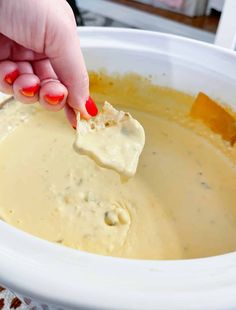 a person dipping cheese into a bowl of soup with a wooden spoon in their hand