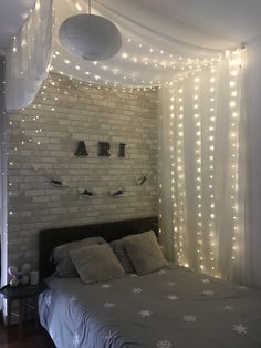 a bed with white lights hanging from the ceiling and curtains on the wall above it