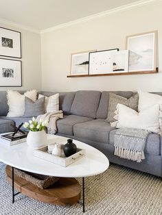 a living room with gray couches and white coffee table in front of pictures on the wall